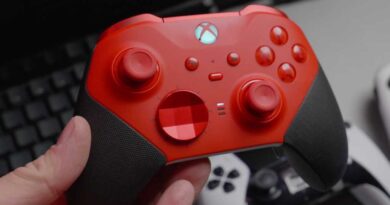 Red wireless Xbox gaming controller in hand held over desk alternate view