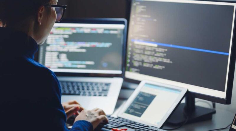 Woman in glasses coding with laptop monitor and tablet