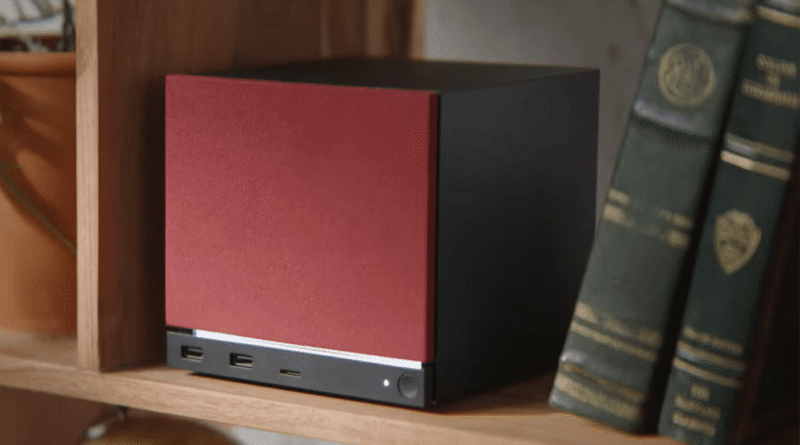 Steam Machine (2026) with red color faceplate on a bookshelf with two green books to its right