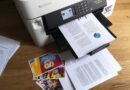 Documents containing text, pie charts, and bar graphs on A4 plain paper, and colour photographs printed on glossy 4x6in photo paper strewn around the Brother MFC-J5340DW inkjet printer