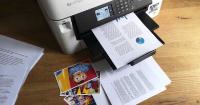 Documents containing text, pie charts, and bar graphs on A4 plain paper, and colour photographs printed on glossy 4x6in photo paper strewn around the Brother MFC-J5340DW inkjet printer