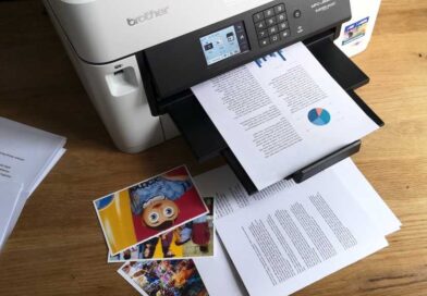 Documents containing text, pie charts, and bar graphs on A4 plain paper, and colour photographs printed on glossy 4x6in photo paper strewn around the Brother MFC-J5340DW inkjet printer
