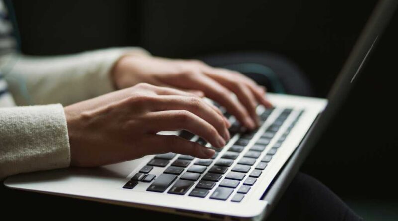 A person with slender hands typing on a laptop