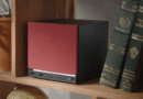 Steam Machine (2026) with red color faceplate on a bookshelf with two green books to its right