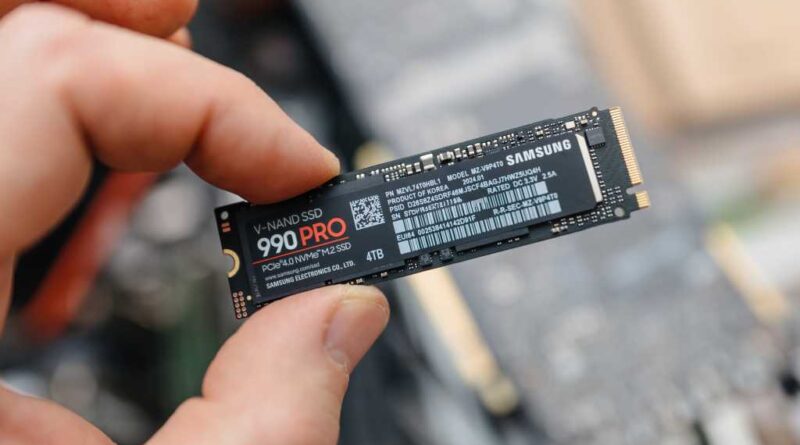 Man holding Samsung 990 PRO SSD between fingers over exposed laptop hero