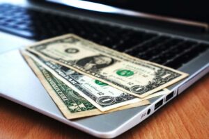 Laptop with black screen and three dollar bills laid out on keyboard