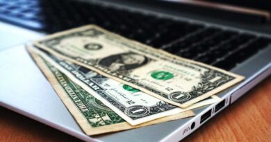 Laptop with black screen and three dollar bills laid out on keyboard