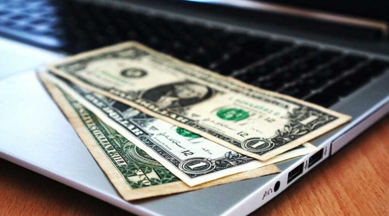 Laptop with black screen and three dollar bills laid out on keyboard