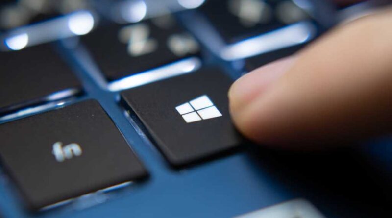 Finger pressing Windows key on a blue laptop keyboard