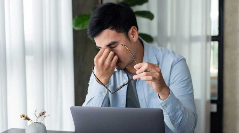 Man pinching tired eyes with glasses off while working at laptop on desk