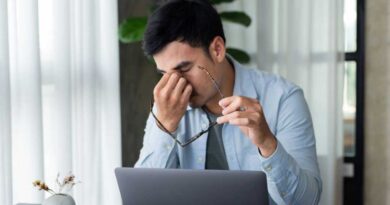 Man pinching tired eyes with glasses off while working at laptop on desk