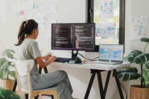 Woman working in home office at desk with laptop and monitor