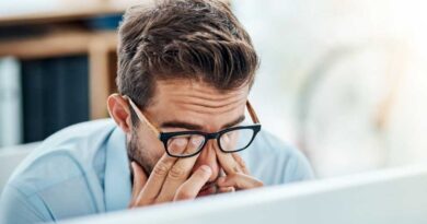 Man with glasses tiredly rubbing eyes while working on a laptop PC