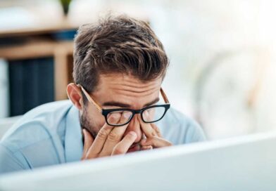 Man with glasses tiredly rubbing eyes while working on a laptop PC