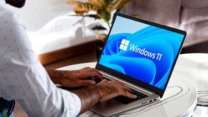 Windows 11 auf einem Laptop auf einem Kaffeetisch mit einem Mann mit Händen auf der Tastatur