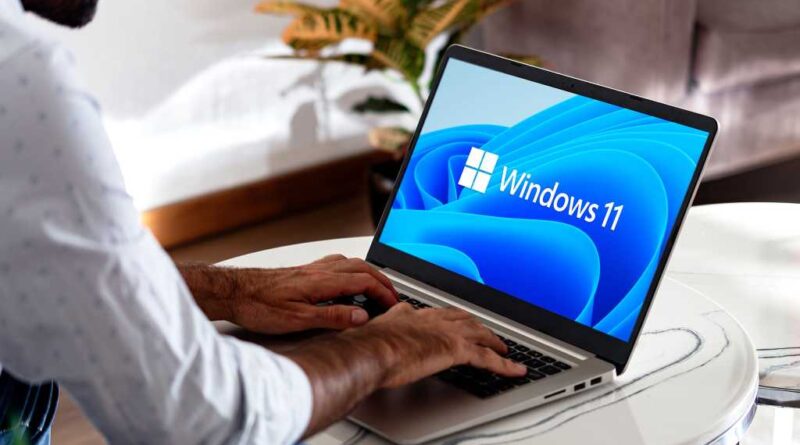 Windows 11 auf einem Laptop auf einem Kaffeetisch mit einem Mann mit Händen auf der Tastatur