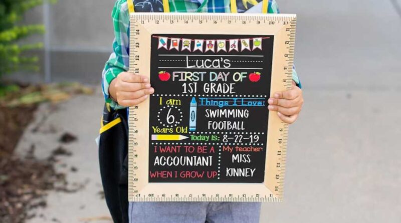 Child holding a "First Day of School" sign board