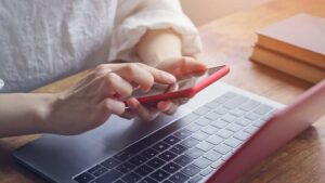 Eine Frau benutzt vor einem Laptop ein Smartphone.
