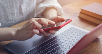 Eine Frau benutzt vor einem Laptop ein Smartphone.