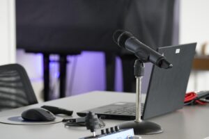 Mann sitzt mit Earover-Kopfhörern vor einem Monitor auf einem Gamerstuhl, Zwei große schwarze Lautsprecher rechts und links vom Monitor.