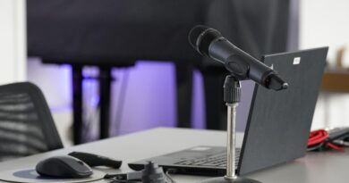 Mann sitzt mit Earover-Kopfhörern vor einem Monitor auf einem Gamerstuhl, Zwei große schwarze Lautsprecher rechts und links vom Monitor.