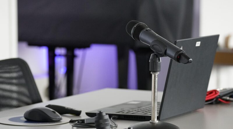 Mann sitzt mit Earover-Kopfhörern vor einem Monitor auf einem Gamerstuhl, Zwei große schwarze Lautsprecher rechts und links vom Monitor.